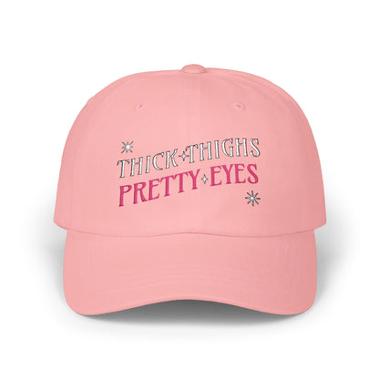 Pink cap with 'THICK THIGHS PRETTY EYES' text on a white background